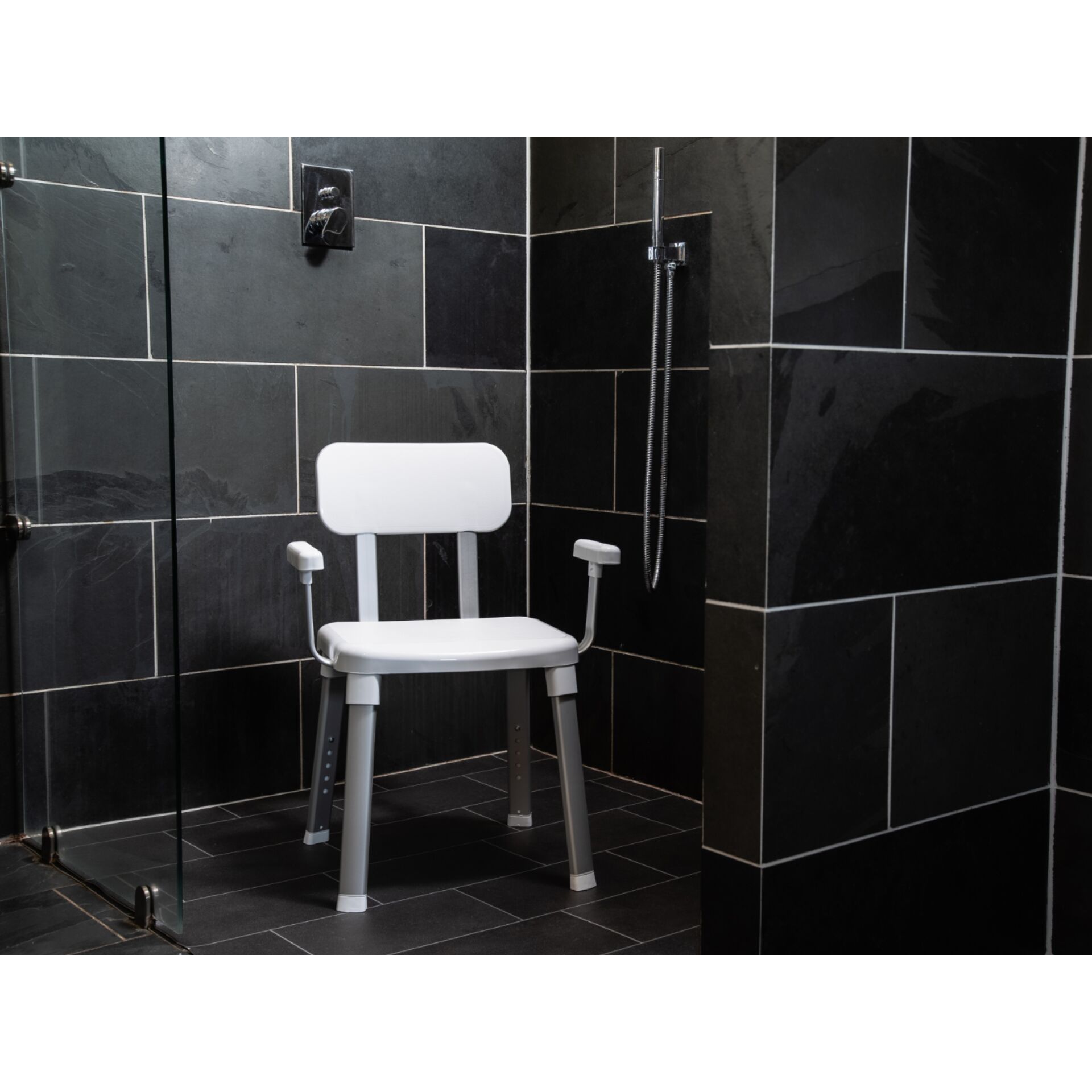 Weißer Duschstuhl mit Rückenlehne und Armlehnen in einer modernen Dusche mit dunklen Fliesen
