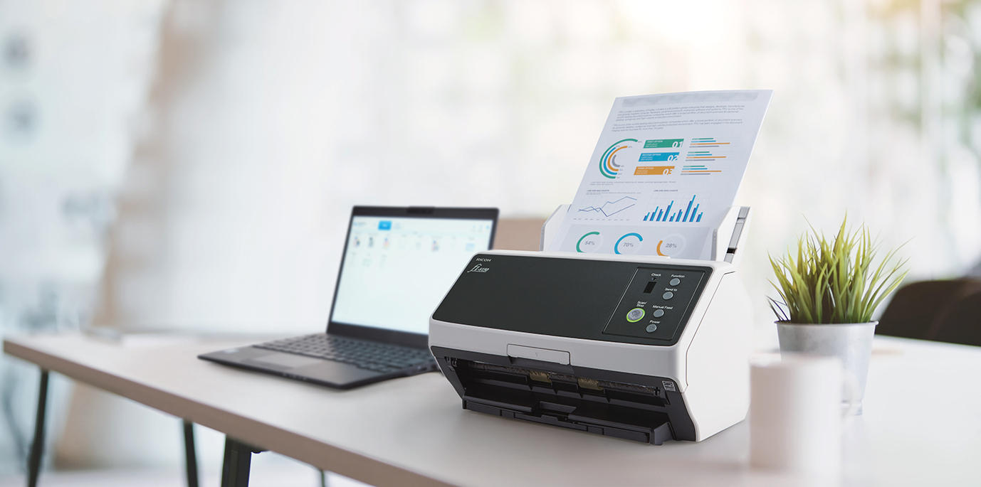 Dokumentenscanner scannt Farbgrafiken neben Laptop im Büro