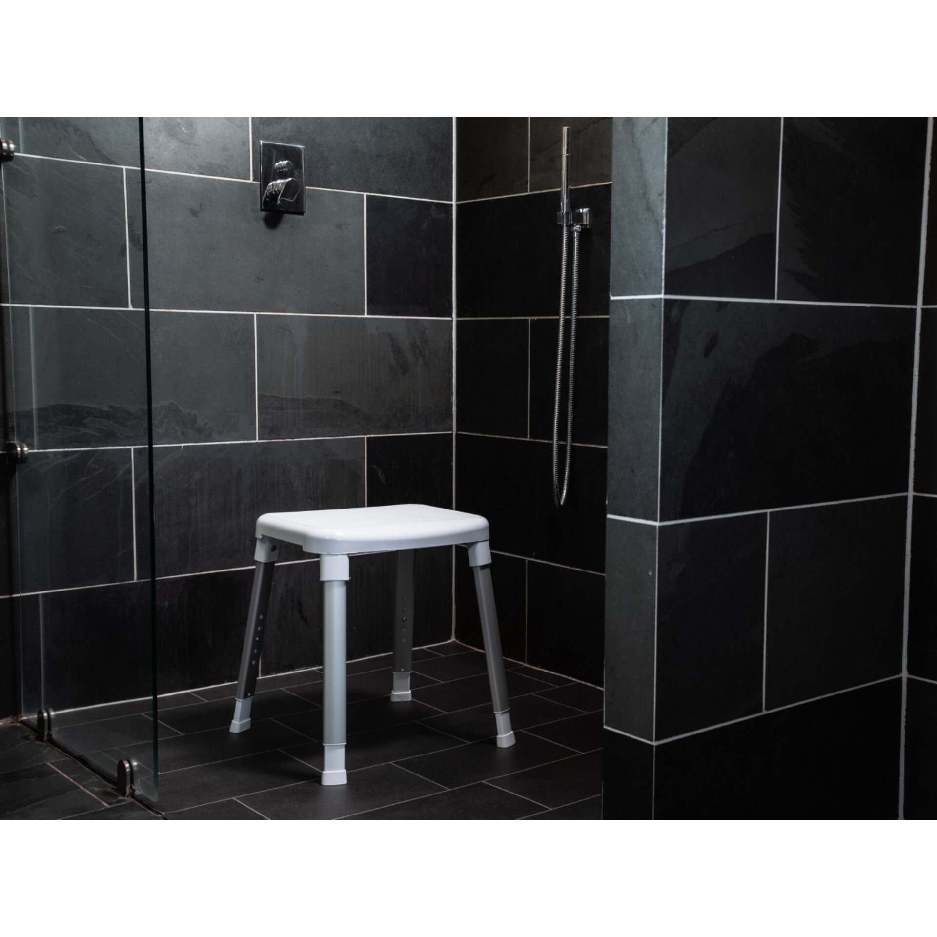 Weißer, höhenverstellbarer Duschhocker in einer schwarz gefliesten Dusche