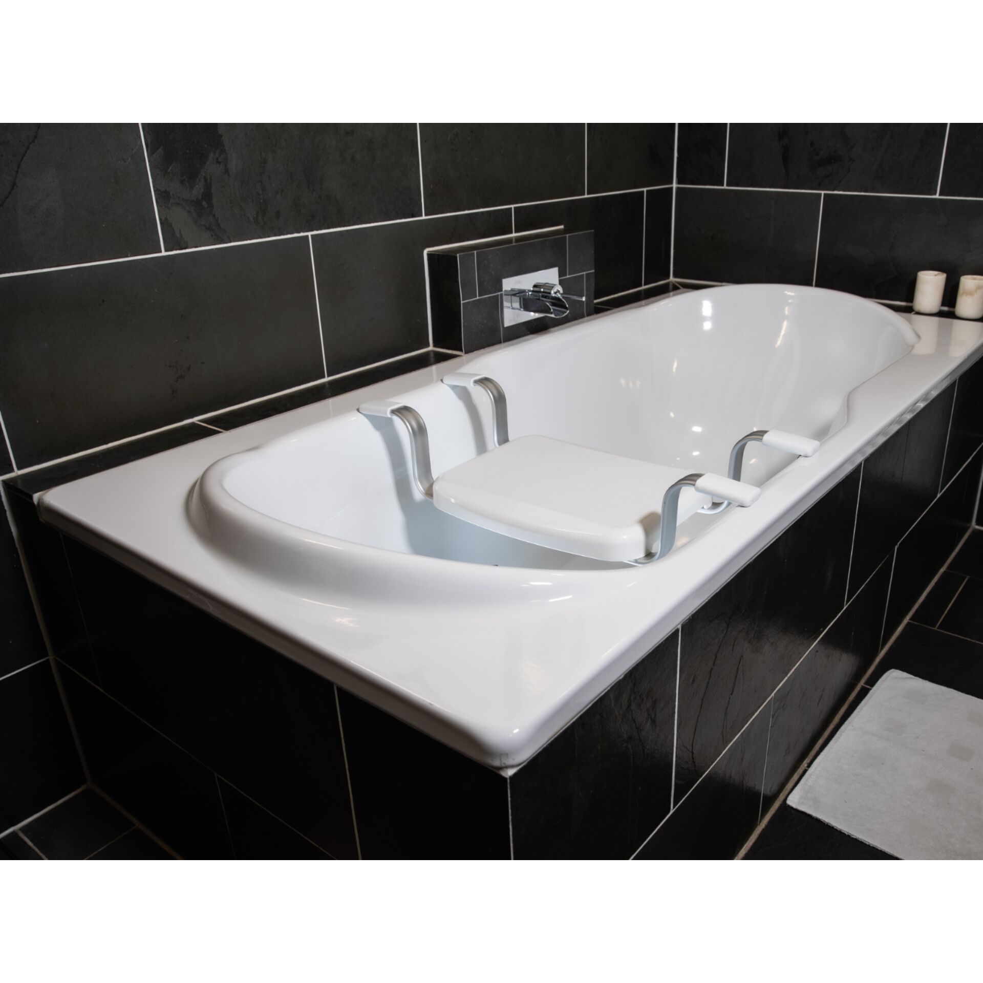 Eine weiße Badewanne mit Badesitz in einem modernen, gefliesten Badezimmer mit dunklen Fliesen.
