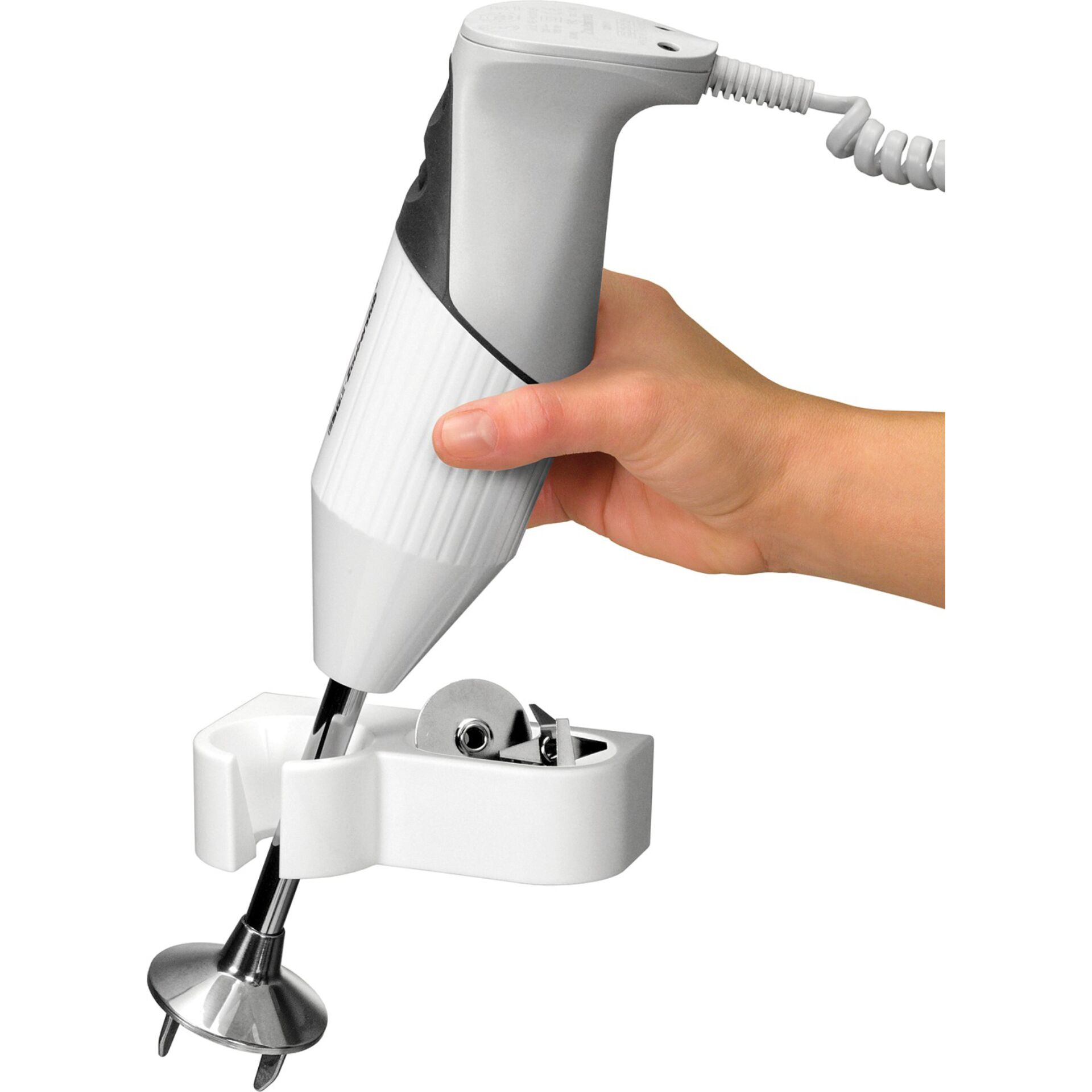 Eine Person hält einen Handmixer, der in einer weißen Halterung mit verschiedenen Aufsätzen befestigt ist.